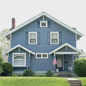 Blue two-story suburban home with white trim and American flag flying on porch column